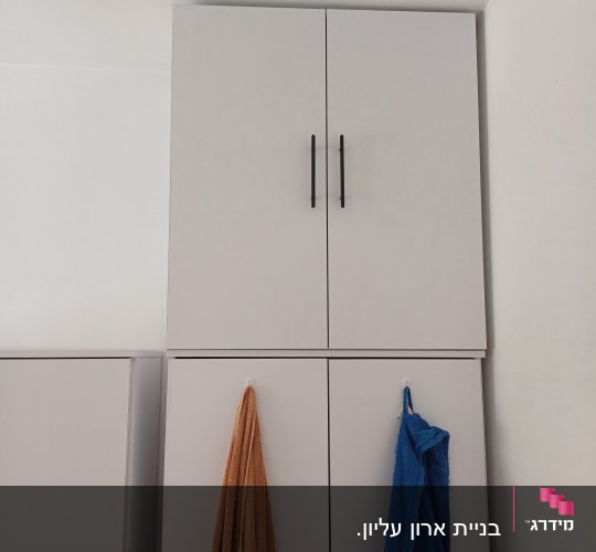 ארון עץ עם ידיות שחורות ומגבות תלויות